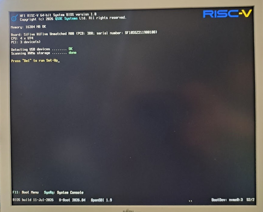 Photograph of the HFI BIOS power-on screen running on a SiFive HiFive Unmatched: the blue RISC-V logo, board and CPU inventory, USB and NVMe enumeration, and the prompt to press Del to run Set-Up.